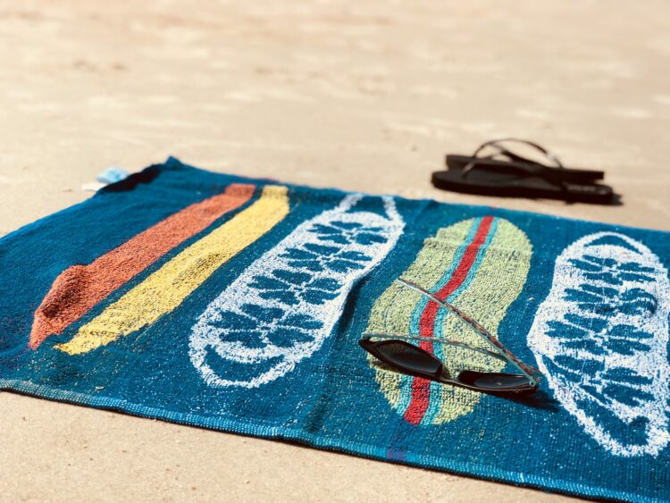 Black sunglasses on blue towel beside pair of black flip flops