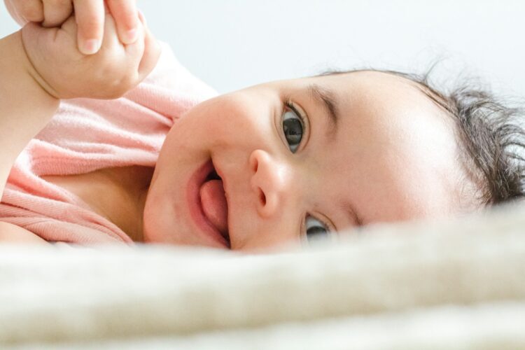 Baby in pink shirt lying on white textile