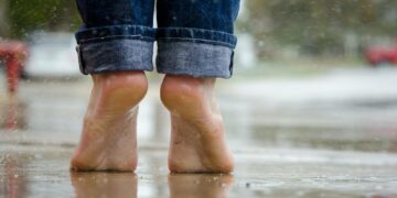 Close-up of bare feet on a wet pavement, capturing calm and connection with nature.