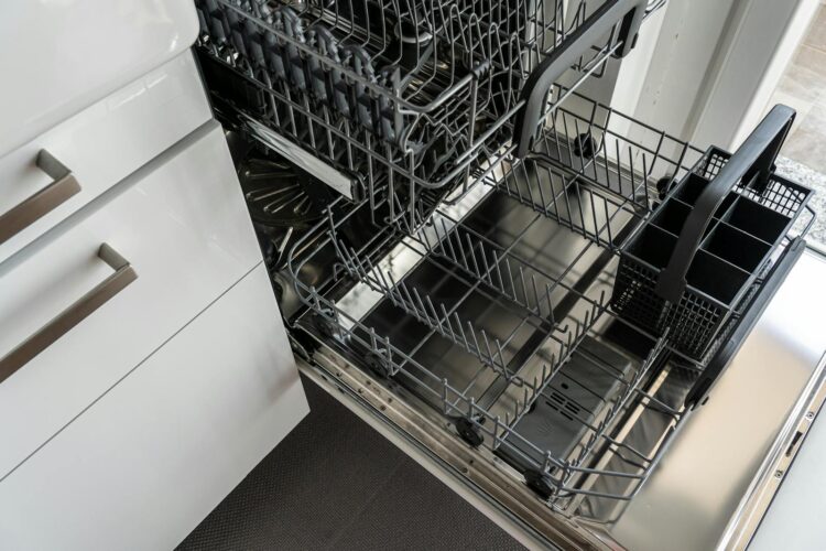 A clean and empty stainless steel dishwasher open in a modern kitchen setting