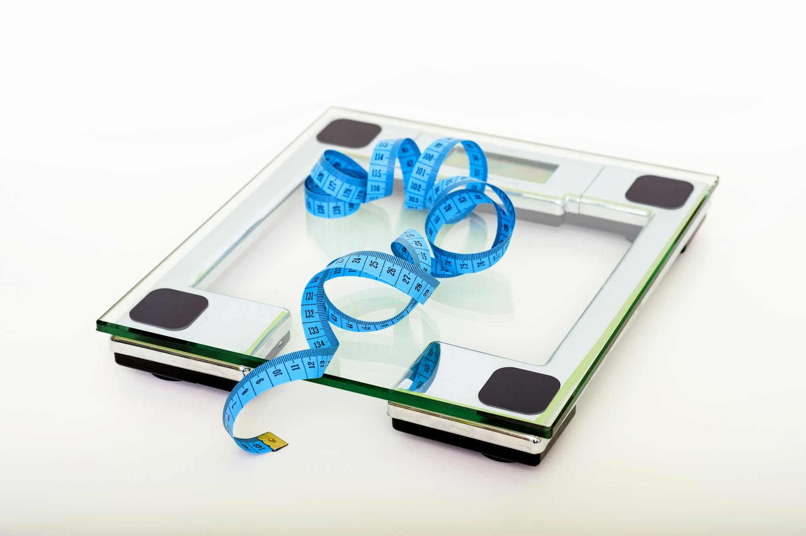 A digital glass weighing scale with a blue measuring tape symbolizing weight management