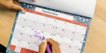 A person marking a calendar in September with a purple pen on a wooden desk.
