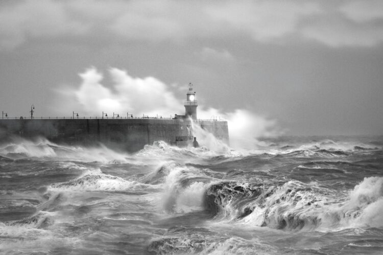 Grayscale photo of sea waves crashing on concrete wall