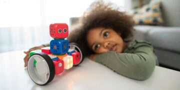 boy lying on bed playing with red and blue toy truck