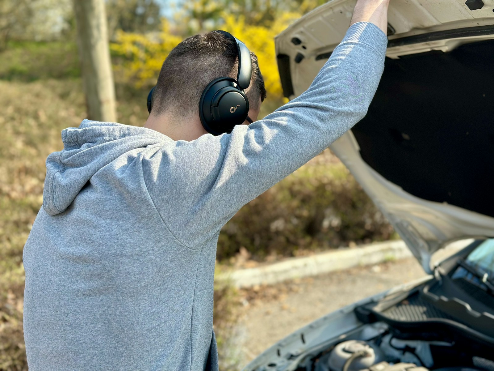 A man with headphones is looking at the hood of a car