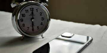 A classic silver alarm clock and modern smartphone placed side by side on a light surface.