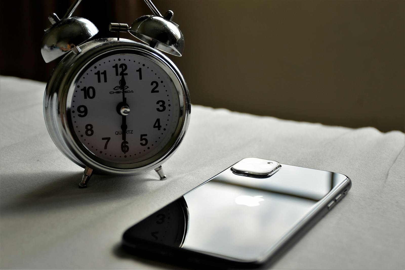A classic silver alarm clock and modern smartphone placed side by side on a light surface