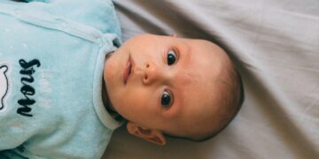 baby in blue onesie lying on white textile