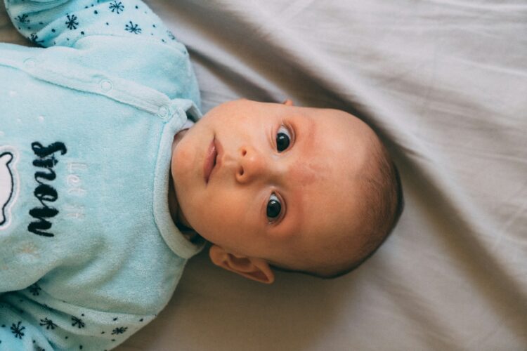 Baby in blue onesie lying on white textile