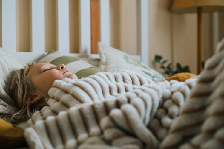 A little girl laying in bed under a blanket