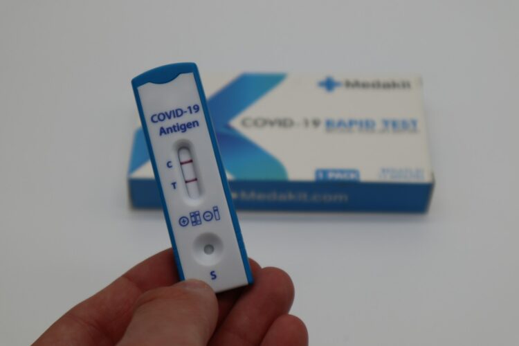 A hand holding a thermometer next to a box of covid   19