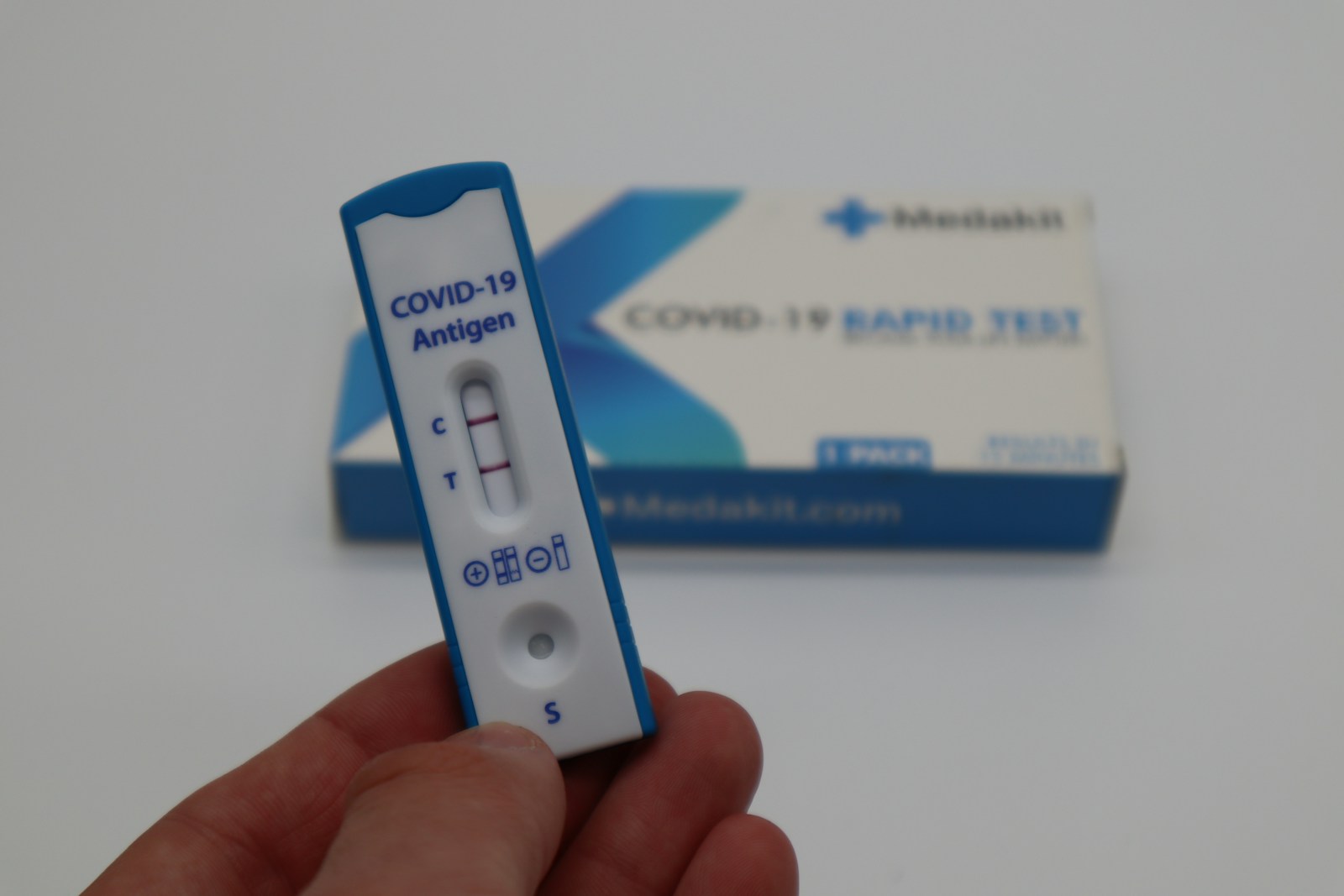 A hand holding a thermometer next to a box of covid   19