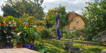 Man walks through a lush garden with a house.