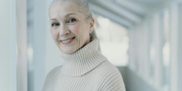 Elegant senior woman with grey hair smiling in a serene indoor setting.