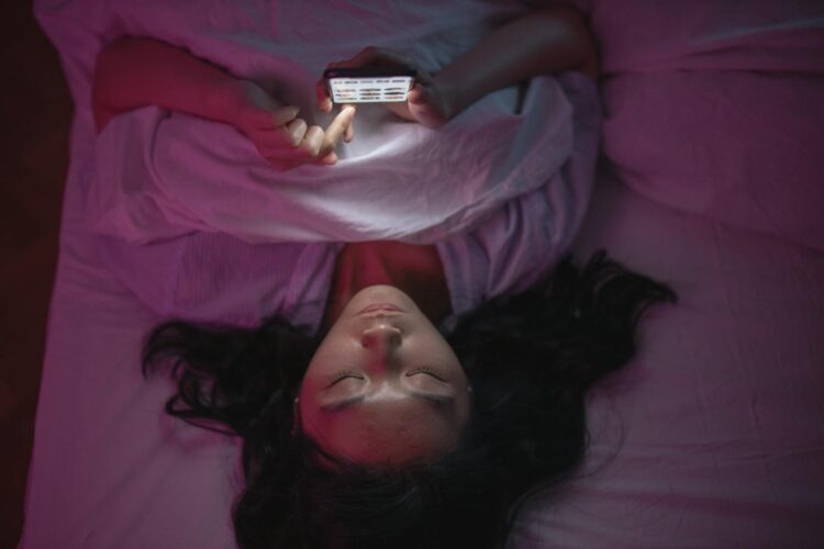 A woman lying in bed at night browsing her smartphone under soft lighting