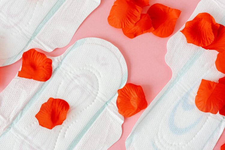 Close up of sanitary pads with red petals on a pink background symbolizing menstruation