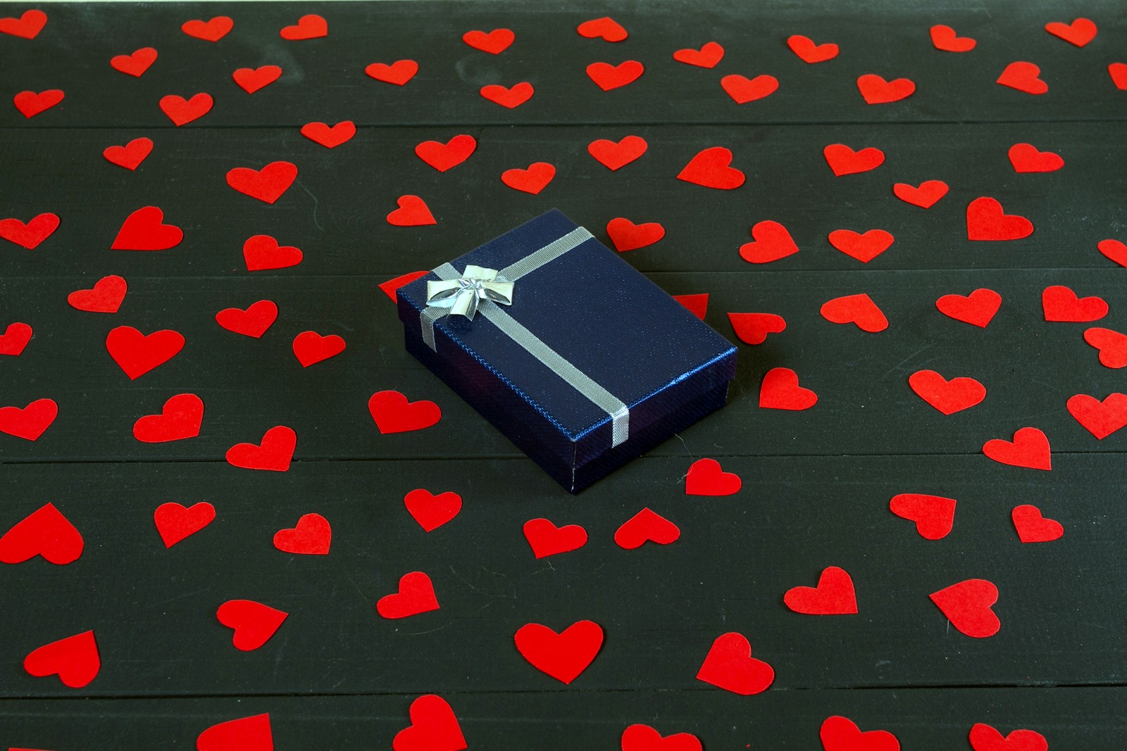 A blue gift box sitting on top of a table covered in hearts