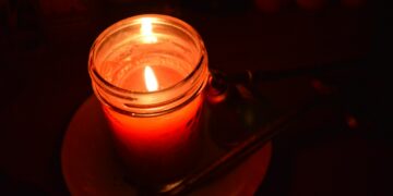 A lit red candle in a glass jar.