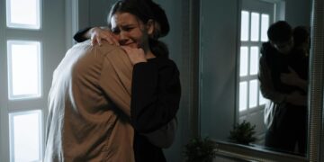 A touching scene of two adults hugging with reflection in mirror, indicating emotional support.