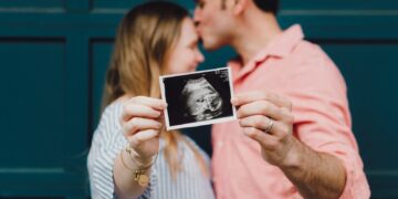 man kissing woman's forehead white holding ultrasound photo