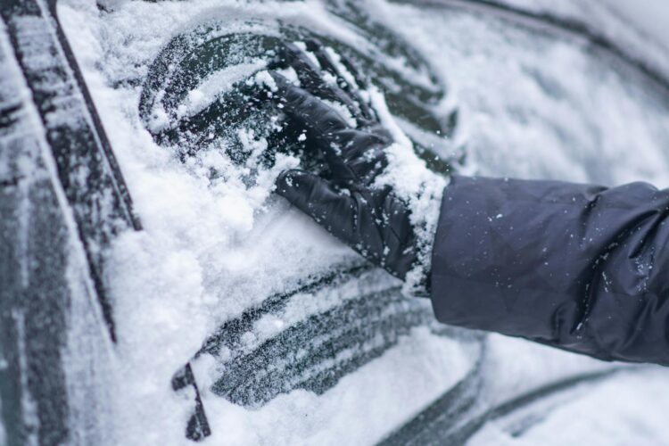 A close up of a gloved hand clearing snow from a car window during winter