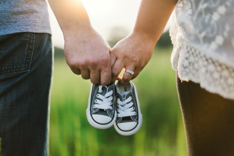 Woman and man holding black crib shoes standing near green grass during daytime