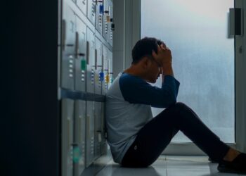 Man in gray long sleeve shirt and black pants sitting on white floor tiles