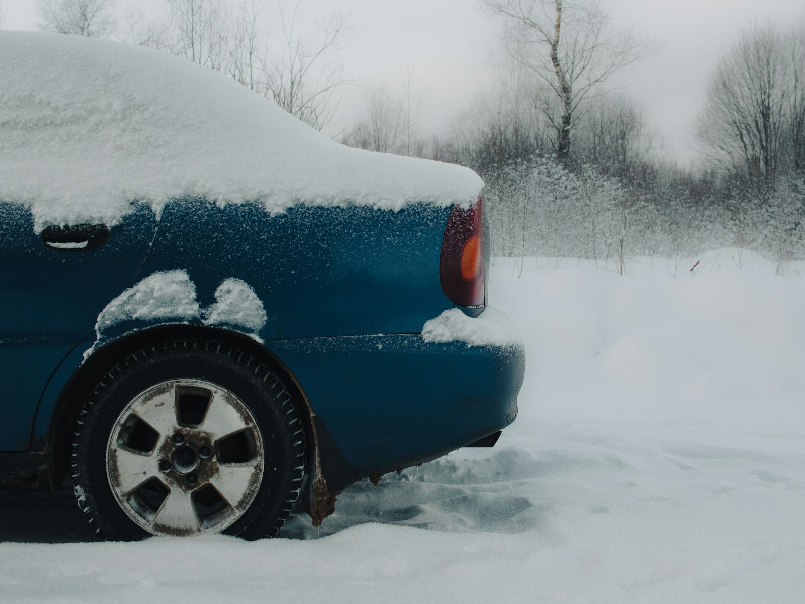A blue car covered in snow on a snowy day