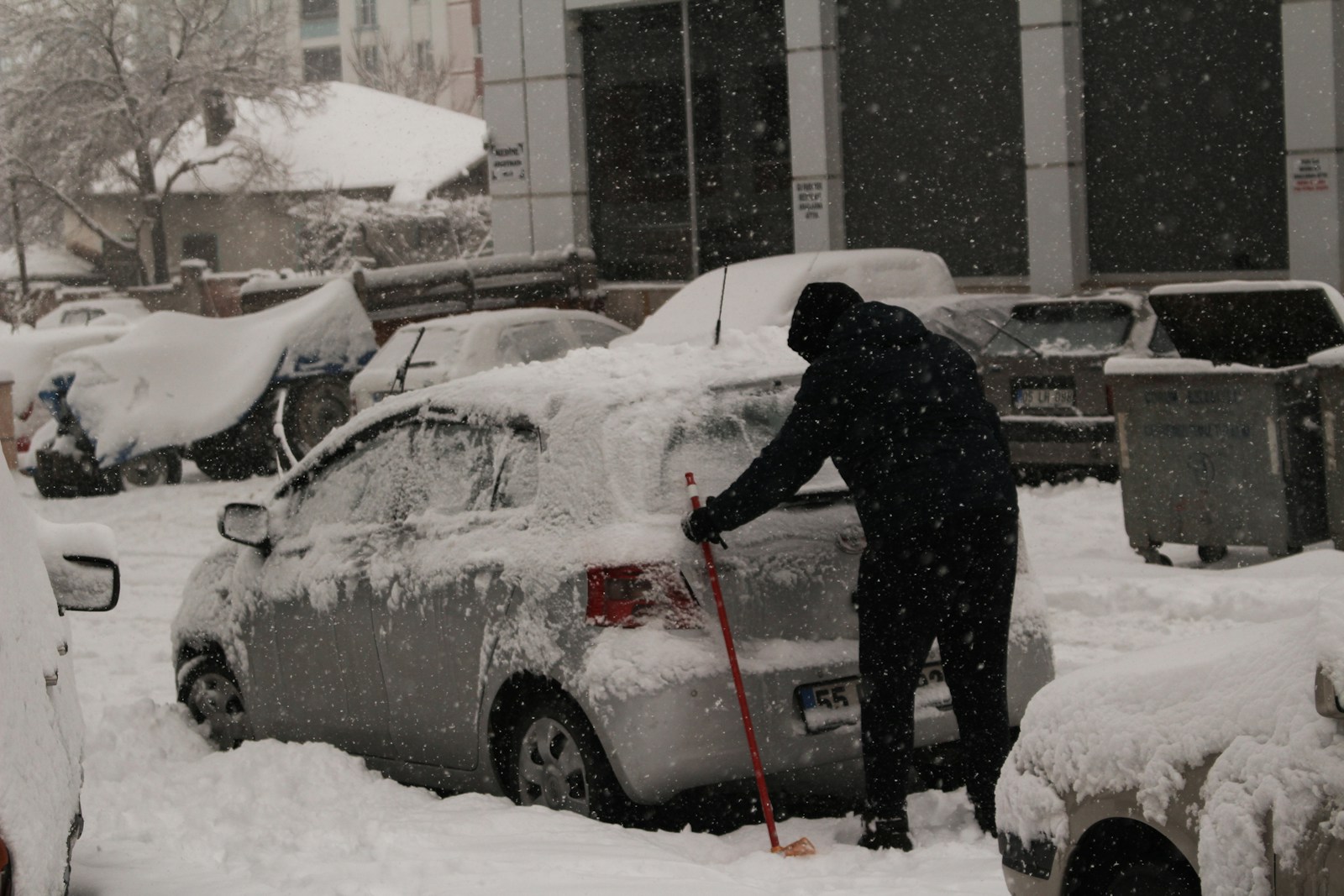 A person shoveling snow off a car