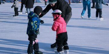 2 children in red jacket and black pants playing ice hockey