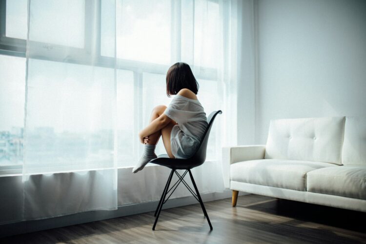 Woman sitting on black chair in front of glass panel window with white curtains
