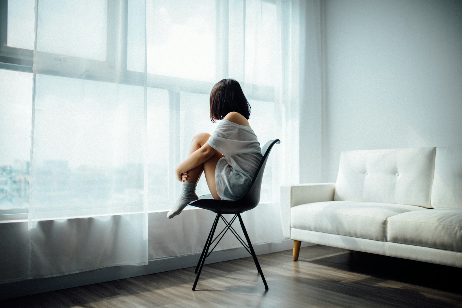 Woman sitting on black chair in front of glass panel window with white curtains