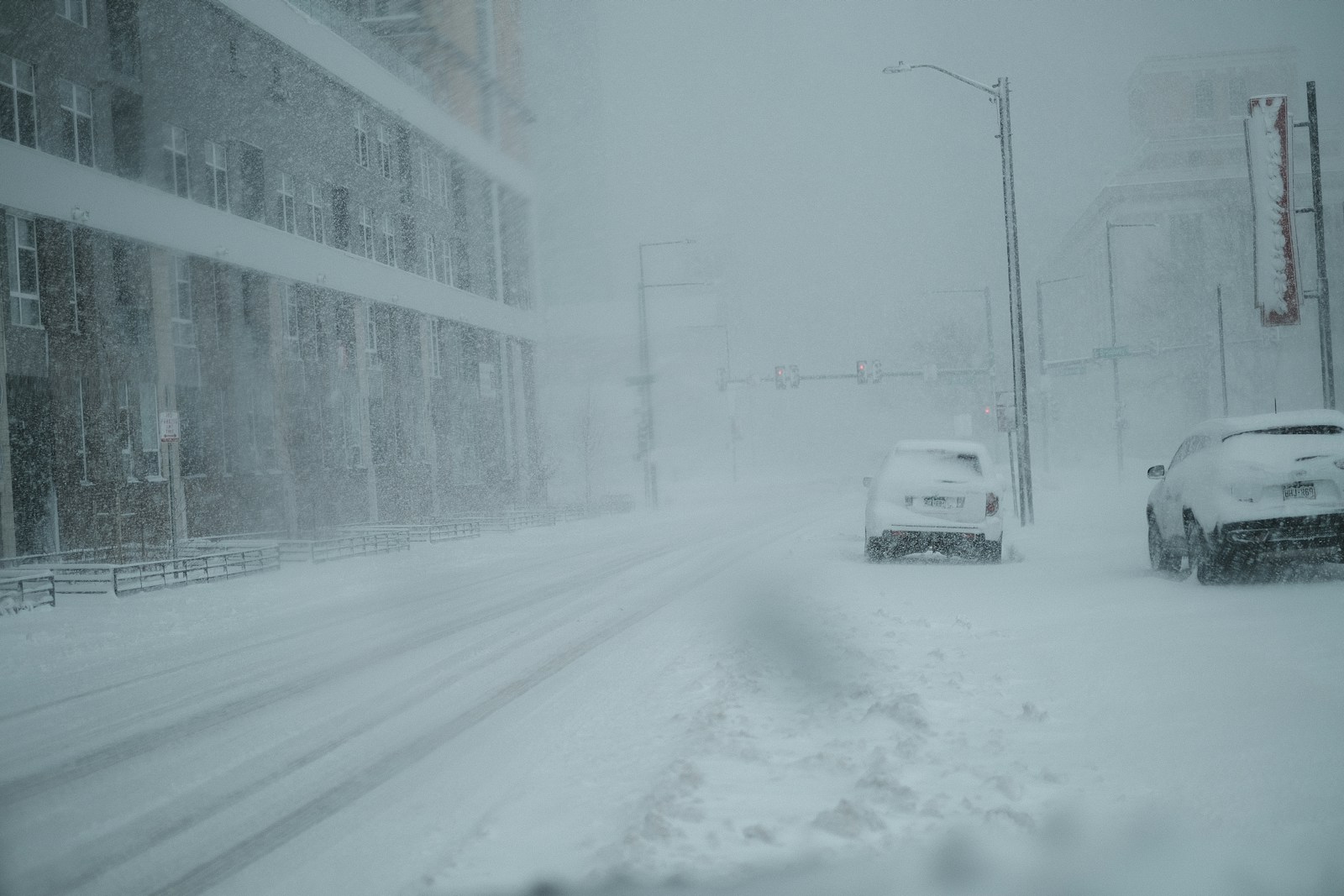 A couple of cars driving down a snow covered street