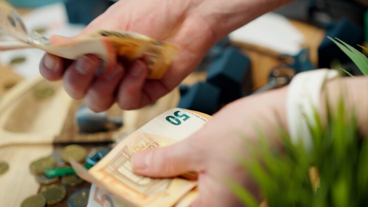 Hands counting euro banknotes with coins scattered around