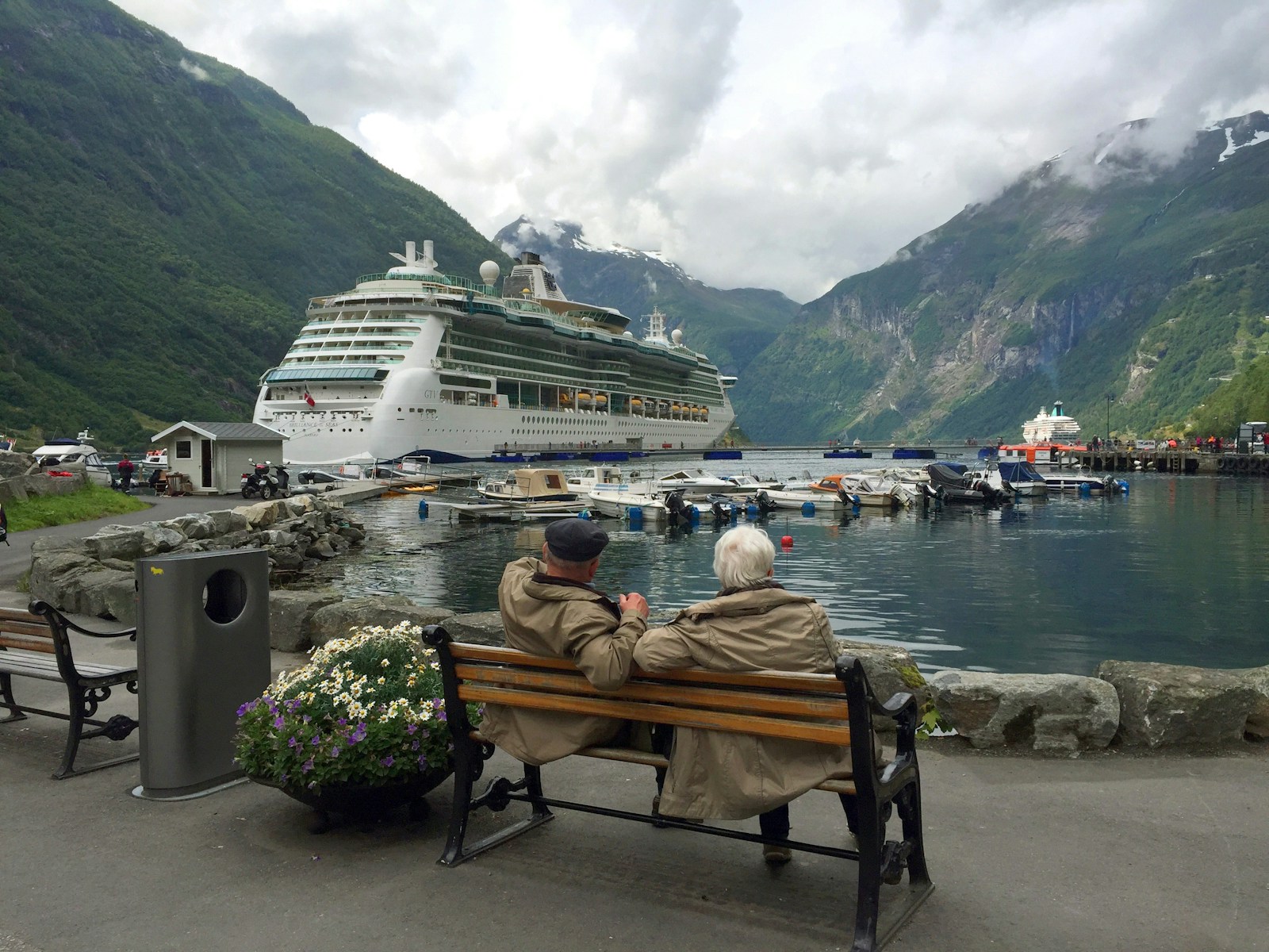Woman in brown coat sitting on brown wooden bench near white cruise ship during daytime