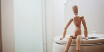 brown wooden doll on white ceramic toilet bowl