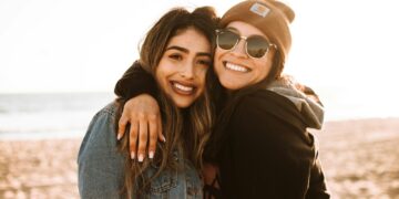 woman hugging other woman while smiling at beach