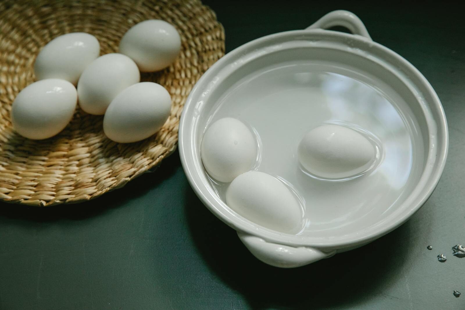 Boiled and raw white eggs arranged in a ceramic bowl and wicker tray on a kitchen surface