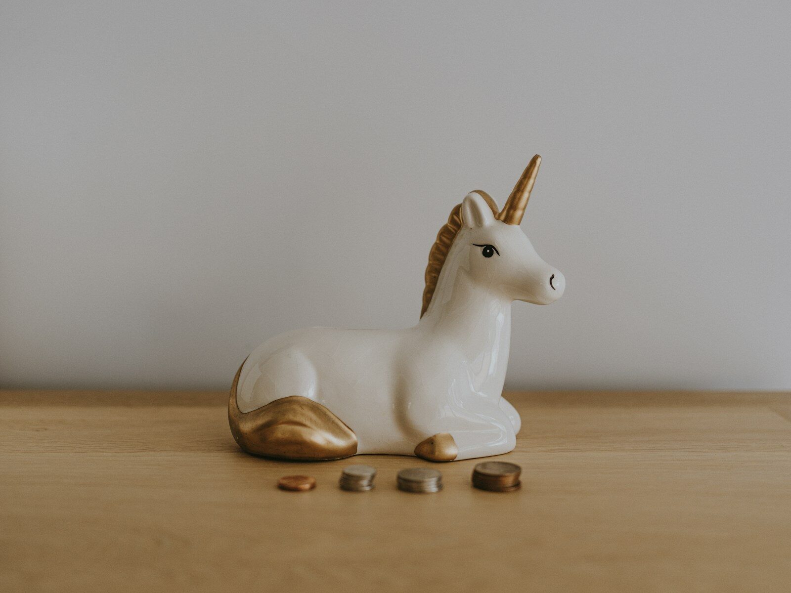 White and gold ceramic unicorn figurine near coins