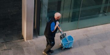 A man pulls a cleaning cart near a building.