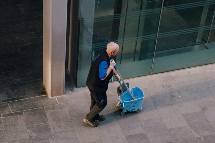 A man pulls a cleaning cart near a building