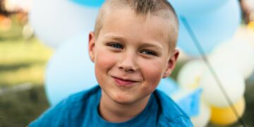 a young boy smiles at the camera with balloons in the background