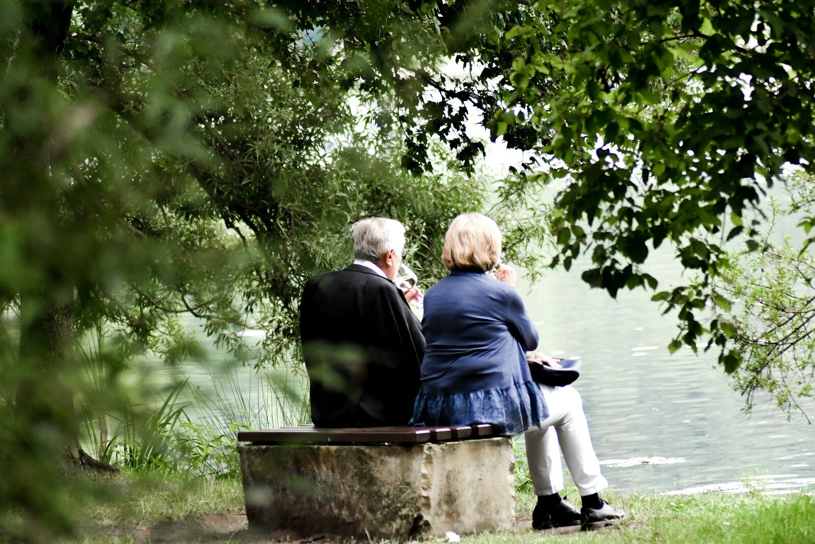 Two people sitting on pavement facing on body of water