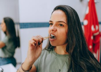 Woman brushing her teeth using a natural toothbrush in a bathroom promoting oral hygiene and sustainability