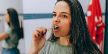 Woman brushing her teeth using a natural toothbrush in a bathroom, promoting oral hygiene and sustainability.