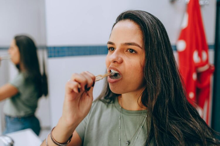 Woman brushing her teeth using a natural toothbrush in a bathroom promoting oral hygiene and sustainability