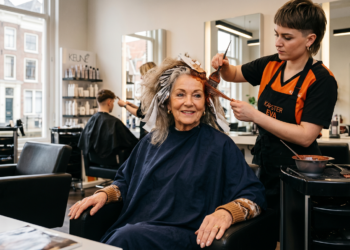 Older woman smiling as a stylist applies hair color with foil in a bright salon setting