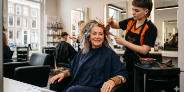 Older woman smiling as a stylist applies hair color with foil in a bright salon setting