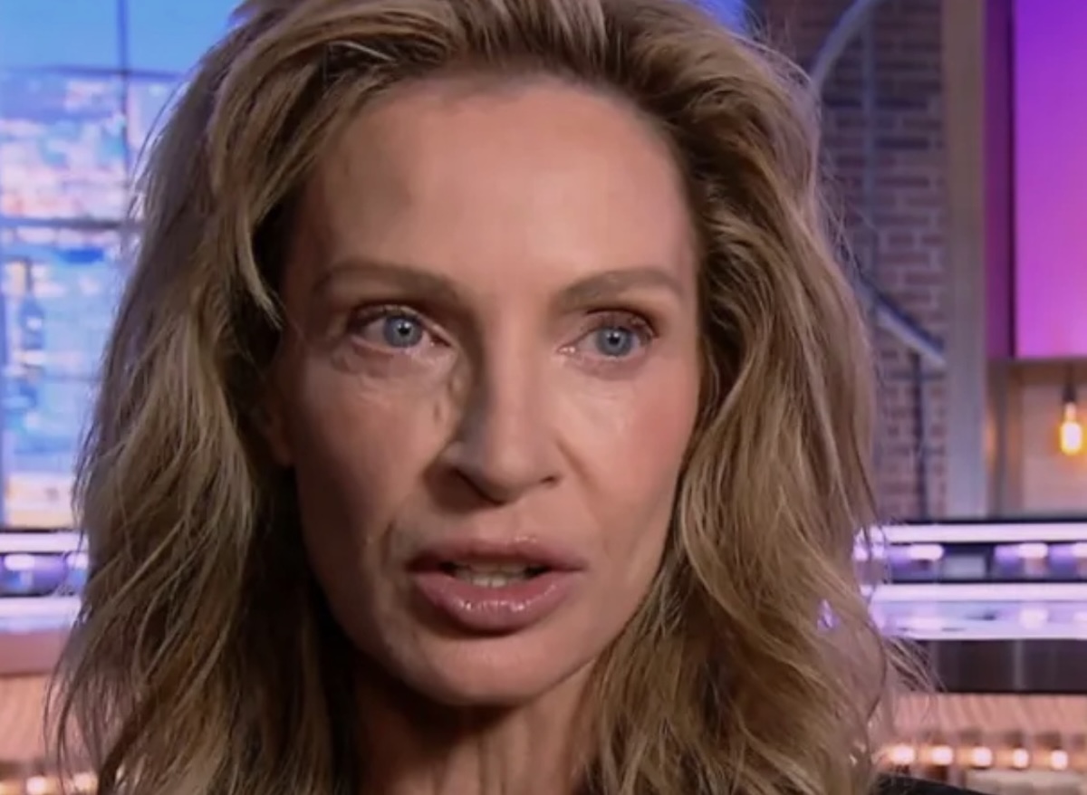 Close up of a woman with long wavy blond hair and blue eyes speaking in a tv studio with blue and purple lighting behind her