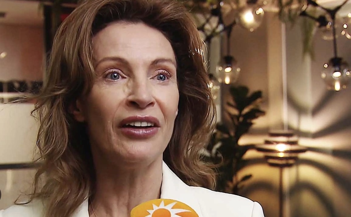 Close up of a woman being interviewed indoors microphone with an orange sun logo in the foreground
